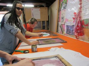 YMCA Academy fashion class students, with Kingi Carpenter, use a silk screening process to design shirts and other materials.