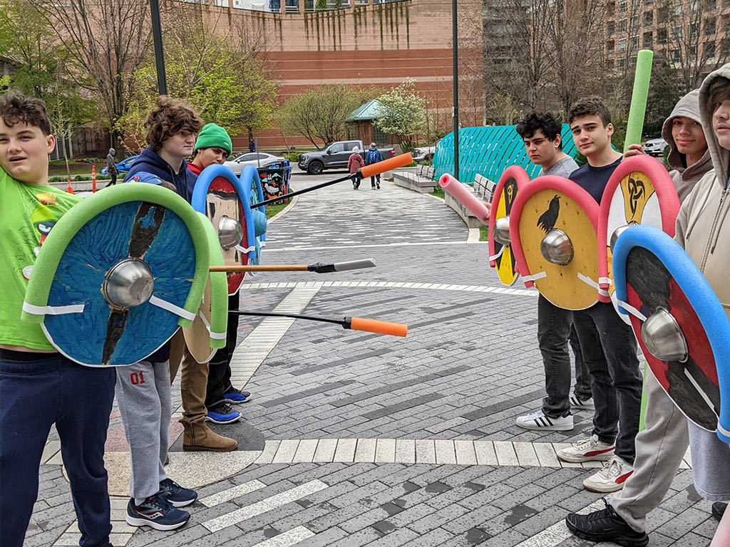 The Grade 12 Adventures in World History class engaged in some hands-on-experiential learning in the park near YMCA Academy. Students have been learning about the adventures of Norwegian, and Danish societies of the Viking Age roughly one thousand years ago.