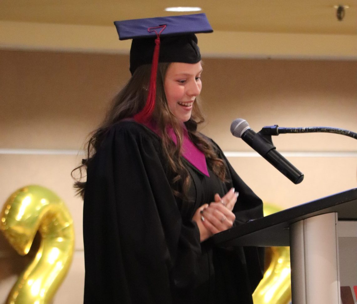 Graduate in cap and gown speaking at podium during ceremony.