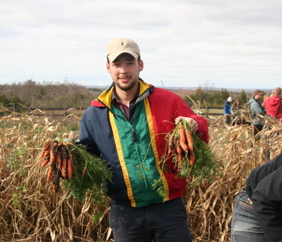 Young man holding freshly harvested carrots at YMCA Academy farm.