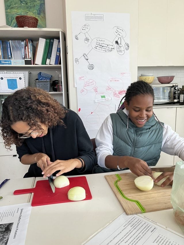 Students cooking and chopping onions in a classroom kitchen setting.