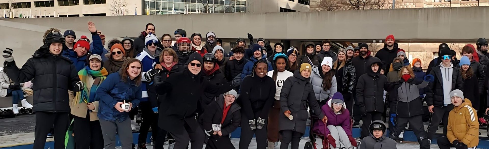 Group of children and adults ice skating at YMCA Academy outdoor rink.