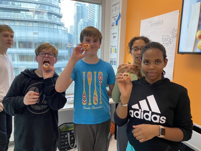 Children at YMCA Academy eating snacks in classroom with city view.