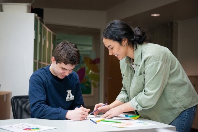 Teacher assisting student with art project at YMCA Academy.