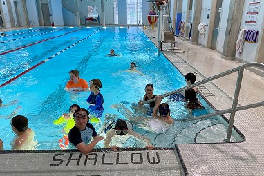 Children swimming and learning in YMCA Academy indoor pool.