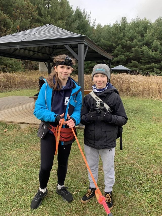 Two smiling kids with outdoor gear at YMCA Academy in nature.