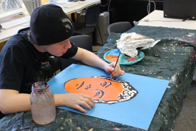 Student painting a colorful portrait at YMCA Academy art class.