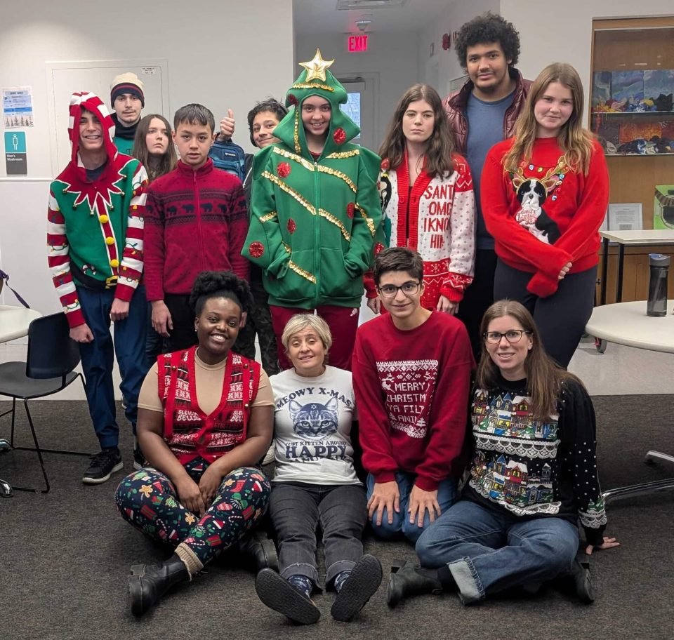 Group of children and teens in festive holiday sweaters and costumes at YMCA Academy.
