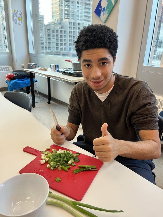 Young student preparing vegetables in a classroom setting at YMCA Academy.