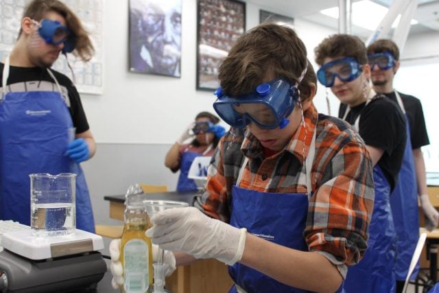 Students conducting a science experiment at YMCA Academy with safety goggles and gloves.