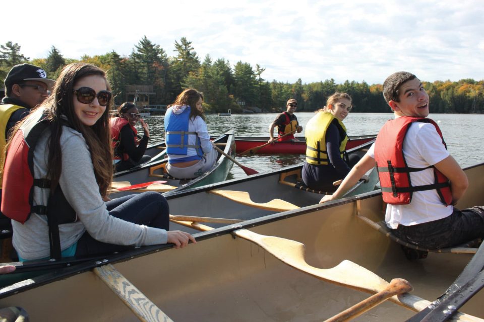 Group of young people canoeing on a lake during YMCA Academy outdoor activity.